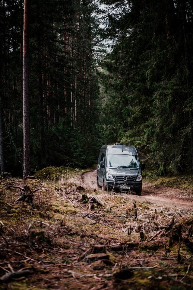 A Mercedes Sprinter van on a rough road in the forest, putting its 4WD to good use.